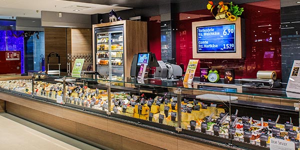 Bildschirme und Waagen mit Produktangeboten und Werbung an der Käsetheke im Supermarkt
