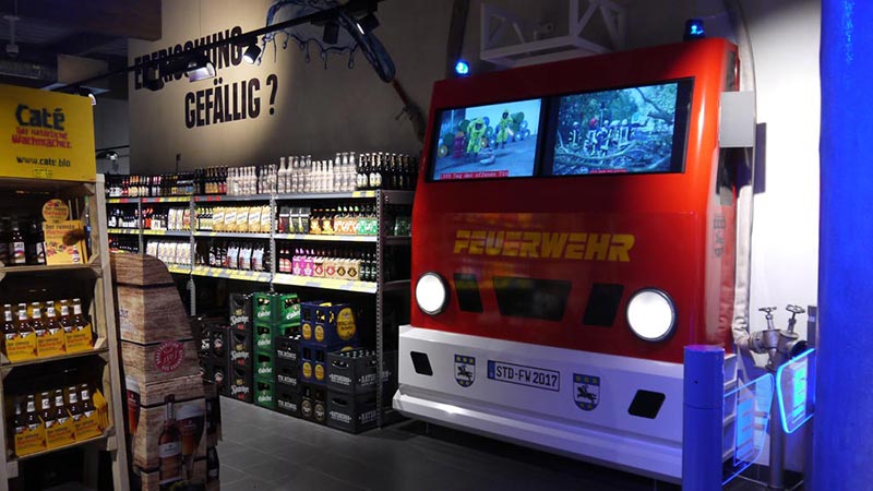 Feuerwehrattrappe mit Bildschirmen statt Frontscheibe im EDEKA Meibohm Getränkemarkt